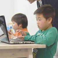 Eita Ide (right) studies computer programming at Kid’s Tech, a newly opened cram school catering to the needs of children with developmental disabilities in Tokyo’s Ota Ward in mid-April. | SATOKO KAWASAKI
