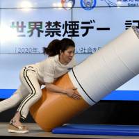 Three-time Olympic women\'s wrestling gold medalist Saori Yoshida tackles a cushion shaped like a cigarette during a World No Tobacco Day event in the Akasaka district in Tokyo on Wednesday. The event was aimed at protecting people\'s health from smoking and passive smoking. | SATOKO KAWASAKI