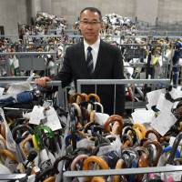 Shoji Okubo, head of the Metropolitan Police Department’s lost and found center in Bunkyo Ward, stands with umbrellas that are waiting to be claimed by their owner. Lost: Struggling to cope with millions of unclaimed items in Tokyo