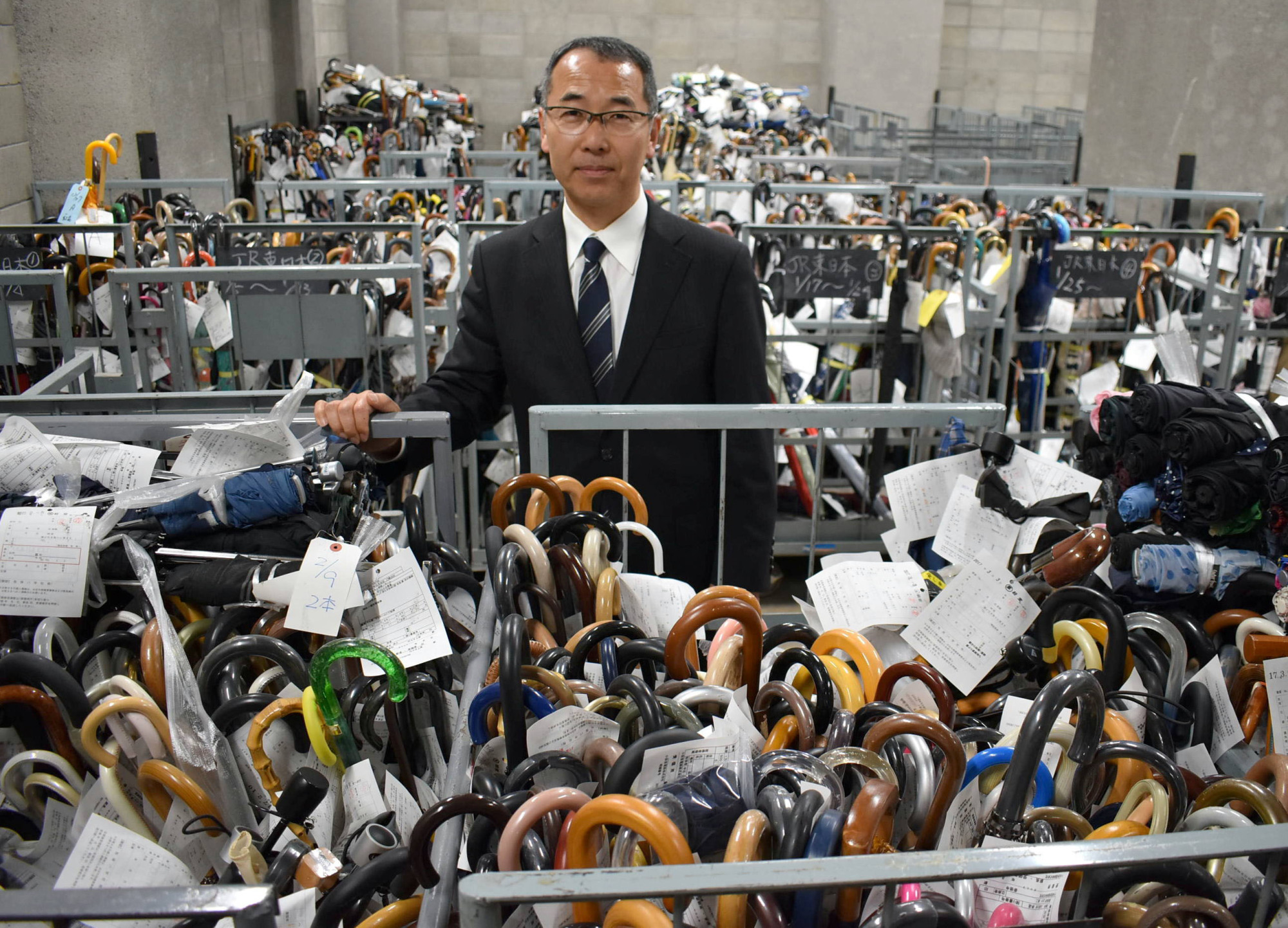 Shoji Okubo, head of the Metropolitan Police Department's lost and found center in Bunkyo Ward, stands with umbrellas that are waiting to be claimed by their owner. | SATOKO KAWASAKI