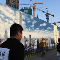 People walk past a construction site in the central business district of Beijing on May 18. Public works spending in China continues to focus on construction and the country has remained the world\'s top builder of skyscrapers for nine years in a row. | AFP-JIJI