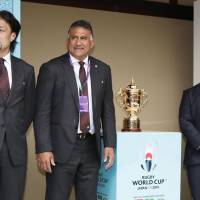 Brave Blossoms head coach Jamie Joseph (center) and players Hitoshi Ono (left) and Shota Horie pose with the Webb Ellis Cup during the Rugby World Cup draw on Wednesday in Kyoto. | KYODO