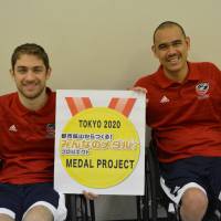 Jeff Butler (left) and Ernie Chun of the United States donate old mobile phones to the Tokyo 2020 Medal Project on Saturday. The project aims to collect materials to be recycled and used in the manufacturing of medals for the Tokyo 2020 Olympics and Paralympics. | JAPANESE PARA-SPORTS ASSOCIATION