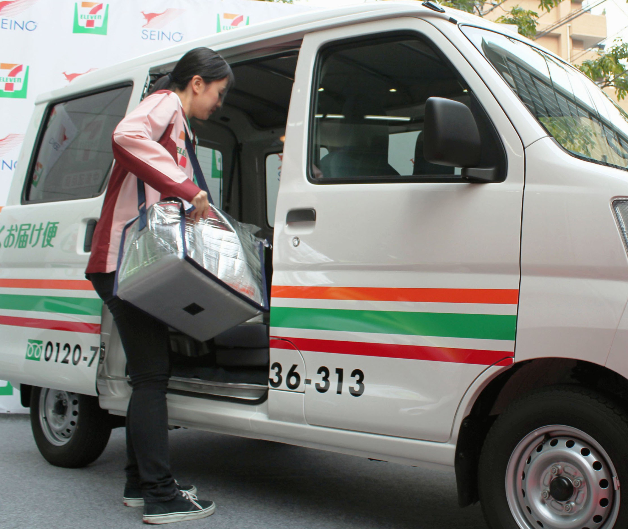 A Seven-Eleven Japan Co. employee demonstrates a delivery service launched in a tie-up with trucking firm Seino Holdings Co. to deliver lunch boxes and other products. | KYODO