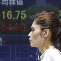 A woman walks by an electronic stock board in Tokyo, Friday. Government panel experts said Japan’s economic expansion continued for 53 months, the third longest in the postwar period. Economy sees Japan's third-longest postwar expansion