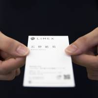 An employee holds a business card made from Limex paper at the TBM Co. headquarters in Tokyo on June 9. TBM produces water- and tree-free paper made from limestone, a rock it proclaims is \"almost inexhaustible.\" | BLOOMBERG