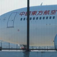 A man stands alongside the damaged engine of a China Eastern Airlines Airbus A330 on the tarmac at Sydney International Airport in Australia Monday after it made an emergency landing with a damaged engine. | REUTERS