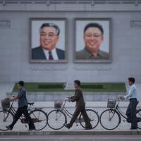 Men push their bicycles past portraits of late North Korean leaders Kim Il Sung and Kim Jong Il in Pyongyang on June 4. | AFP-JIJI
