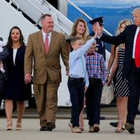U.S. President Donald Trump, flanked by the families of businesspeople he claims were harmed by Obamacare, high-fives a young boy as he arrives to deliver remarks on the U.S. health care system at Cincinnati Municipal Lunken Airport in Cincinnati, Ohio, Wednesday. | REUTERS