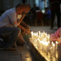 A man holds back tears as he lights candles for victims of an attack at the Resorts World Manila complex Friday in Manila. Philippine police seek casino attacker's identity