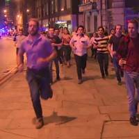 In this image taken from video footage, people run from the scene of attack, alongside a man strolling holding a pint of beer (right) in London late Saturday. People in the U.K. have responded to the deadly London Bridge attack with sorrow and distinctly British humor, hailing the man pictured walking away from the mayhem holding a pint of beer as a tongue-in-cheek symbol of defiance. | SKY NEWS / VIA AP