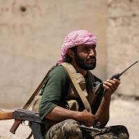 A Syrian Democratic Forces (SDF) fighter carries his weapon and a walkie-talkie in Raqqa\'s western neighborhood of Jazra, Syria, Sunday. | REUTERS