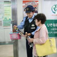 An Osaka Prefectural Police officer hands out a flyer warning about money transfer scams near an ATM in Higashiosaka on Monday. | KYODO