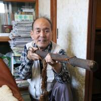 Retired high school teacher Koichi Saito uses a container of arrows to demonstrate how to use a mokuju in this photo taken recently in Tsushima, Aichi Prefecture. | CHUNICHI SHIMBUN