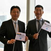 Naosuke Fujita (left), managing director, and Hiroki Inaba, vice president of Goldman Sachs Japan Co.\'s legal department, pose with flags they placed in the office to show their solidarity with LGBT employees at the firm\'s head office in Tokyo. | SATOKO KAWASAKI