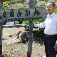 Mandarin orange farmer Shoji Yamamoto stands by a sign pointing to his orchard on Teshima Island in Kagawa Prefecture. | KYODO
