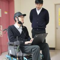 Makoto Sasaki (right), an assistant professor at Iwate University, helps test a wheelchair that can be operated by the user\'s tongue movements. | KYODO