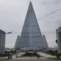 People walk past the 105-story pyramid-shaped Ryugyong Hotel in Pyongyang Friday. Walls set up to keep people out of a construction area around the gargantuan Ryugyong Hotel were pulled down as the North marked the anniversary of the Korean War armistice to reveal two broad new walkways leading to the building and the big red propaganda sign declaring that North Korea is a leading rocket power. With rocketry plug, Pyongyang opens area near giant 'pyramid' hotel 30 years in making but still unoccupied