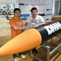 Takahiro Inagawa (left), the president of Interstellar Technologies Inc., a space venture based in Hokkaido, shakes hands with its founder President Takafumi Horie alongside a model of their rocket MOMO in Tokyo on Thursday. | KYODO