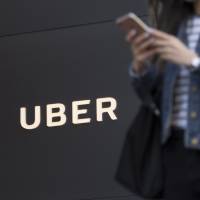 A pedestrian checks a mobile device in front of the Uber Technologies Inc. headquarters building in San Francisco last month. | BLOOMBERG