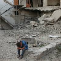 A boy sits near rubble of damaged buildings in Arbin, a town in the Damascus countryside, Tuesday. At least 11 civilians reported killed as airstrikes blamed on regime hit Syria truce town
