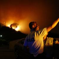 Police officers gesture next to a fire blazing in Biguglia, on the French Mediterranean island of Corsica, on Monday. | AFP-JIJI