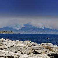 Smoke rises from wildfires burning on the slopes of Mount Vesuvius volcano as the Castel dell\'Ovo castle in seen in the foreground, in Naples, Italy, Wednesday. Firefighters are battling wildfires throughout southern Italy, including along the slopes of the volcano Vesuvius. | CIRO FUSCO / ANSA / VIA AP