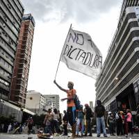 An opposition activist hols a flag reading \"No more dictatorship\" during a blockade to protest Venezuelan President Nicolas Maduro in Caracas on Tuesday. Venezuela\'s government on Tuesday defiantly brushed aside U..S President Donald Trump\'s threat of economic sanctions by saying it will go ahead with the election of a controversial body to rewrite the country\'s constitution. | AFP-JIJI