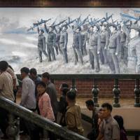 People walk up stairs near a propaganda poster depicting Korean People\'s Army soldiers at a museum in Sinchon, south of Pyongyang, on Saturday. North Korea said Sunday that its latest ICBM test was a \"warning\" targeting the U.S. for its efforts to slap new sanctions on Pyongyang and threatened a counterstrike if provoked militarily by Washington. | AFP-JIJI