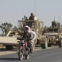 Syrian citizens ride their motorcycle past U.S. armored vehicles on a road that links to Raqqa city in northeast Syria Wednesday. The U.S. has up to 1,000 troops in Syria mostly involved in training and advising the local forces against IS. Kurdish forces have gained confidence in light of open U.S. support to their forces, particularly as the battle for Raqqa took off. Civilian deaths mount as U.S.-backed Syria force purges half of Raqqa of Islamic State fighters