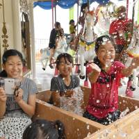 Children play while riding a merry-go-round featuring bathtubs instead of seats at a temporary amusement park in Beppu, Oita Prefecture, on Saturday. | KYODO