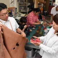 Katsunori Sagawa (left) looks at a pair of babies’ shoes made of wild boar skin at a workshop in Date, Fukushima Prefecture. Date goes whole hog into boar leather business in Fukushima