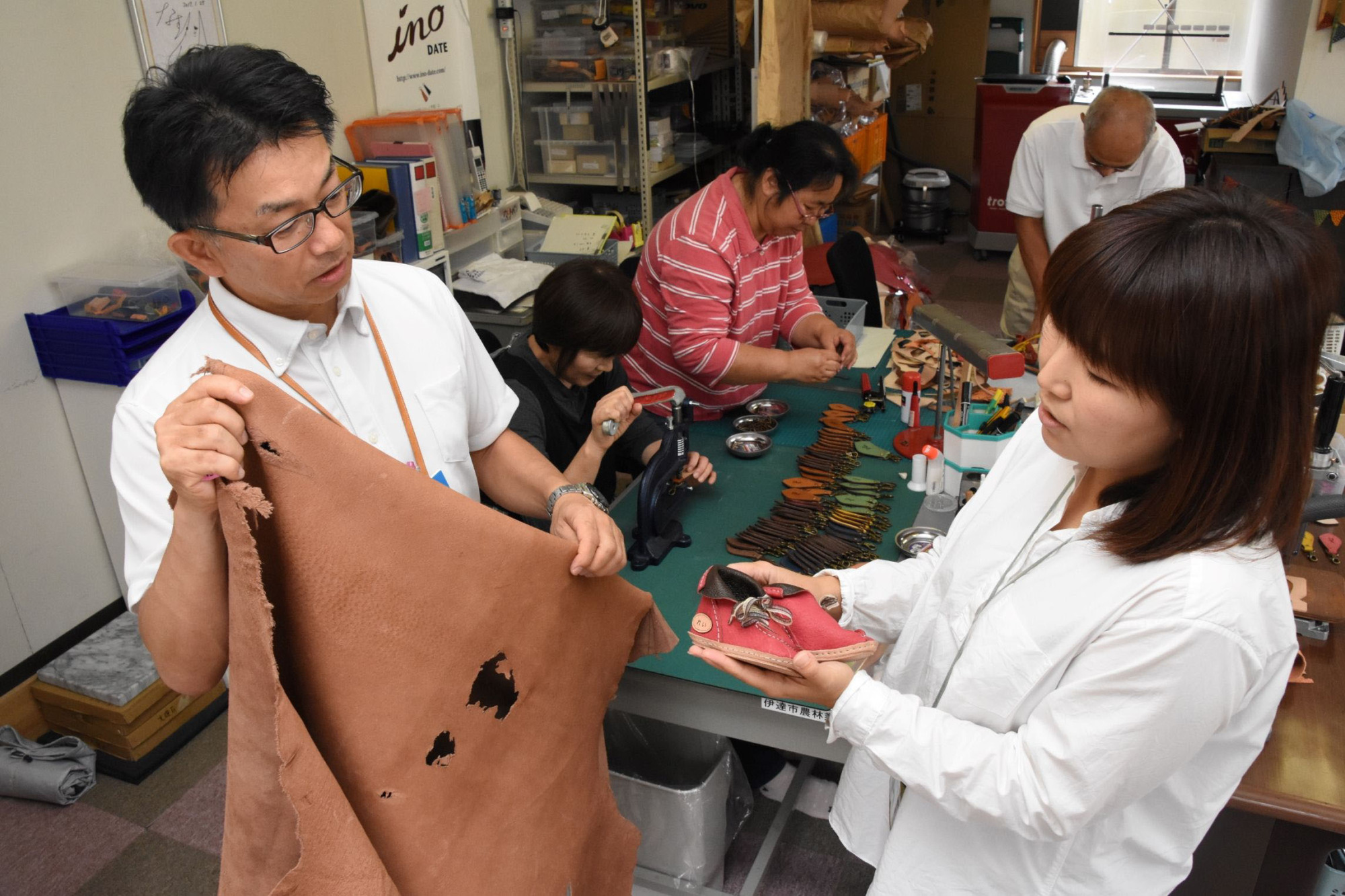 Katsunori Sagawa (left) looks at a pair of babies' shoes made of wild boar skin at a workshop in Date, Fukushima Prefecture. | FUKUSHIMA MINPO