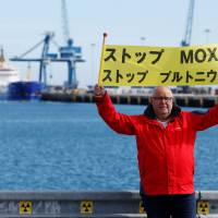 Yannick Rousselet of Greenpeace demonstrates against radioactive MOX (mixed oxide fuel) as the ship Pacific Egret (background) is set to travel to Japan with a container of MOX, on Tuesday at the port of Cherbourg-Octeville, northwestern France. In France, anti-nuclear activists protest sixth MOX shipment en route to Japan