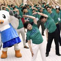 Tokyo Gov. Yuriko Koike and other metropolitan government officials kick off a daily exercise routine at City Hall on Monday to mark the three-year countdown to the opening of the 2020 Olympics. | KYODO