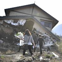 People approach a wrecked house in Kumamoto Prefecture on the first anniversary of the fatal April 2016 earthquakes. Early Sunday, Kumamoto was hit by a temblor measuring lower 5 on the Japanese intensity scale to 7. | KYODO