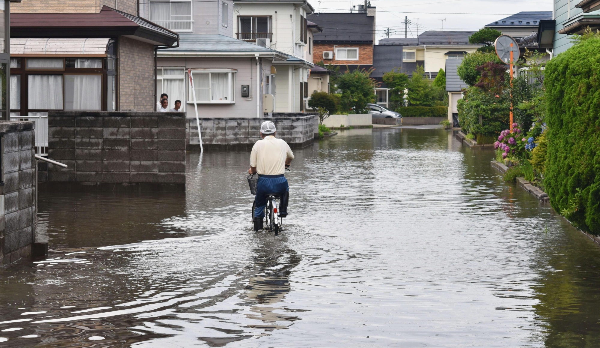 A man rides his bicycle through floodwaters in the city of Akita on Sunday. | KYODO