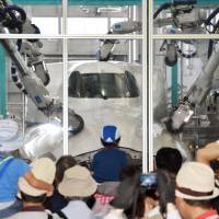 Shinkansen fans watch the long arms of a robot tasked with polishing the train\'s distinctively shaped nose during an event in Hamamatsu, Shizuoka Prefecture, on Saturday. | KYODO