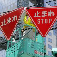 A traffic sign is replaced with a bilingual one in Osaka on Saturday. | KYODO