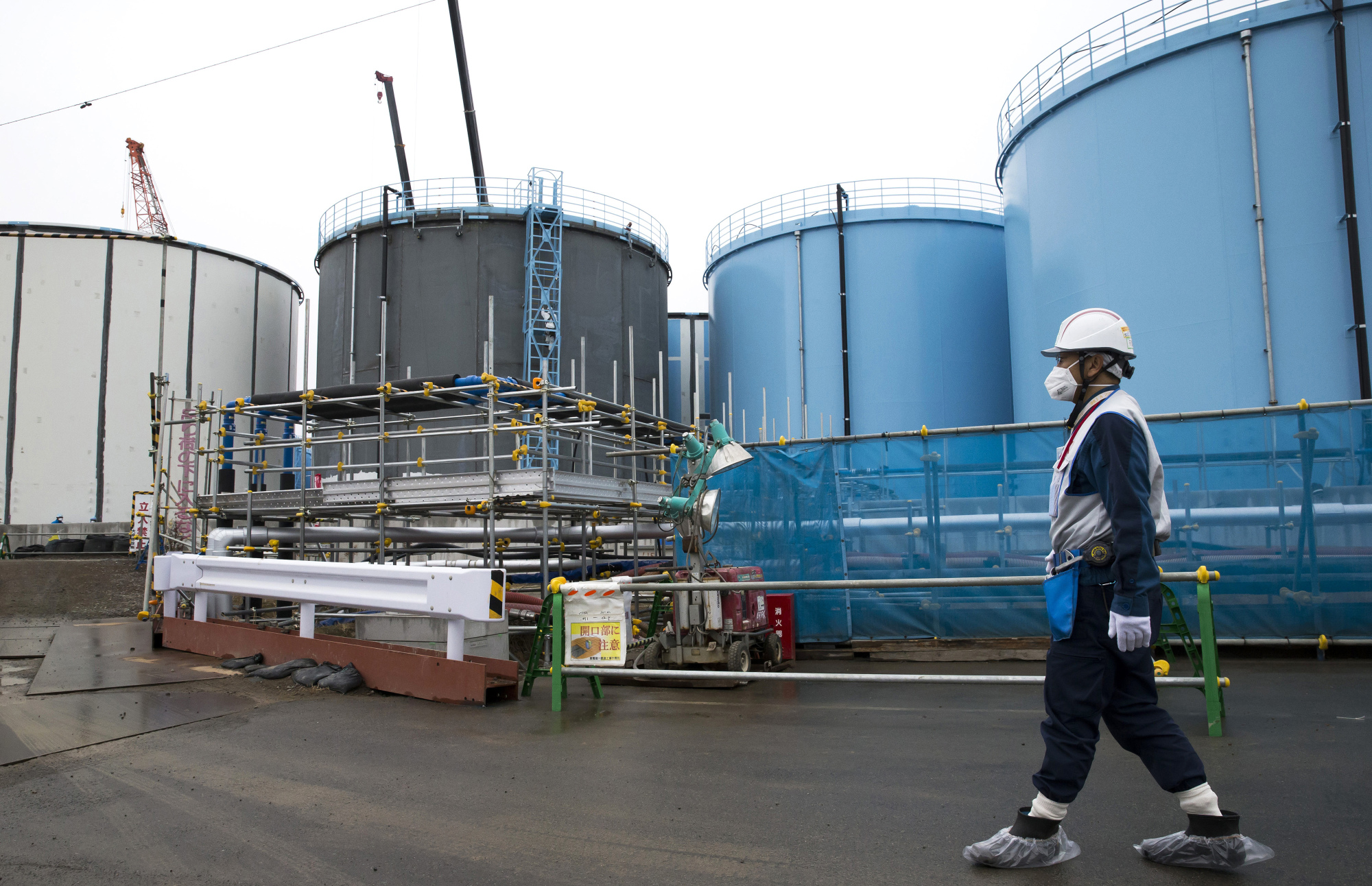 An employee walks past storage tanks for contaminated water at the tsunami-crippled Fukushima No. 1 nuclear power plant of the Tokyo Electric Power Co. in Okuma, Fukushima Prefecture, in February. Tepco needs to release the water &#8212; which contains radioactive tritium that is not removable but considered not harmful in small amounts &#8212; into the Pacific Ocean, Chairman Takashi Kawamura said. | TOMOHIRO OHSUMI / POOL PHOTO / VIA AP, FILE