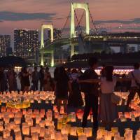People stand amongst paper lanterns while looking out at Rainbow Bridge in Odaiba Marine Park in Tokyo on July 17. Foreign tourists spent a record ¥2.05 trillion in the half-year period up 8.6 percent from the previous year. | AFP-JIJI
