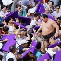 Yokozuna Hakuho heads to the locker room as three-time world figure skating champion Mao Asada and other fans take cover from thrown cushions after his defeat on the 11th day of the Nagoya Grand Sumo Tournament. | KYODO