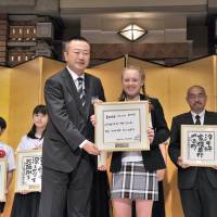 Thirteen-year-old Briton Gracie Starkey receives a framed copy of her winning poem in the English haiku category (\"Freshly mown grass/ clinging to my shoes/ my muddled thoughts\") from Itoen President Daisuke Honjo at the 28th Itoen Oi Ocha New Haiku Contest at Imperial Hotel Tokyo on July 6. | YOSHIAKI MIURA