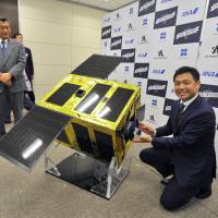 Mitsunobu Okada (right), founder and CEO of Astroscale, on Friday shows off a model of the new ELSA-d satellite designed to capture orbiting space debris. Astroscale hopes to launch the device sometime in 2019. | YOSHIAKI MIURA
