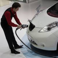 An employee prepares to install a charging plug in the socket of a Nissan Leaf electric automobile during the Geneva International Motor Show in the Swiss city in 2015. | BLOOMBERG