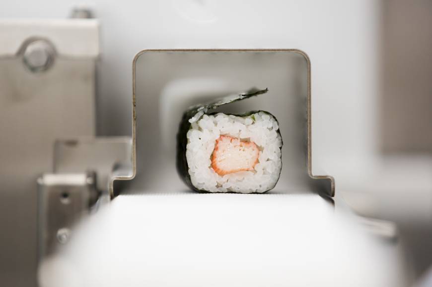 A roll of maki-sushi exits a Suzumo Machinery Co. sushi machine during a demonstration at the company
