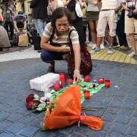 A woman on Friday places a candle next to the first flowers and a message to the victims at the spot where a van plowed into a crowd on Thursday in Barcelona. Five Barcelona attack suspects killed
