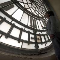 A House of Commons staff member poses for a photograph Thursday in front of one of the deteriorating faces of the Great Clock ahead of planned renovation work on Elizabeth Tower at the Houses of Parliament, part of the Palace of Westminster, in London. As Brexit looms, Britons fret over Big Ben clock's four-year silence