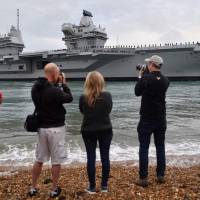 People line the shore to watch as tug boats maneuver the 65,000-ton British aircraft carrier HMS Queen Elizabeth into Portsmouth Harbor in Portsmouth, southern England on Wednesday, as it arrives at for the first time in her home port. Britain's new aircraft carrier HMS Queen Elizabeth arrives at Portsmouth port