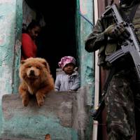 Armed Forces members patrol, as residents watch, during an operation against organized crime in the Manguinhos slum complex in Rio de Janeiro Monday. Brazilian military, police raid Rio's violent favelas but not before soldier tips off gangs